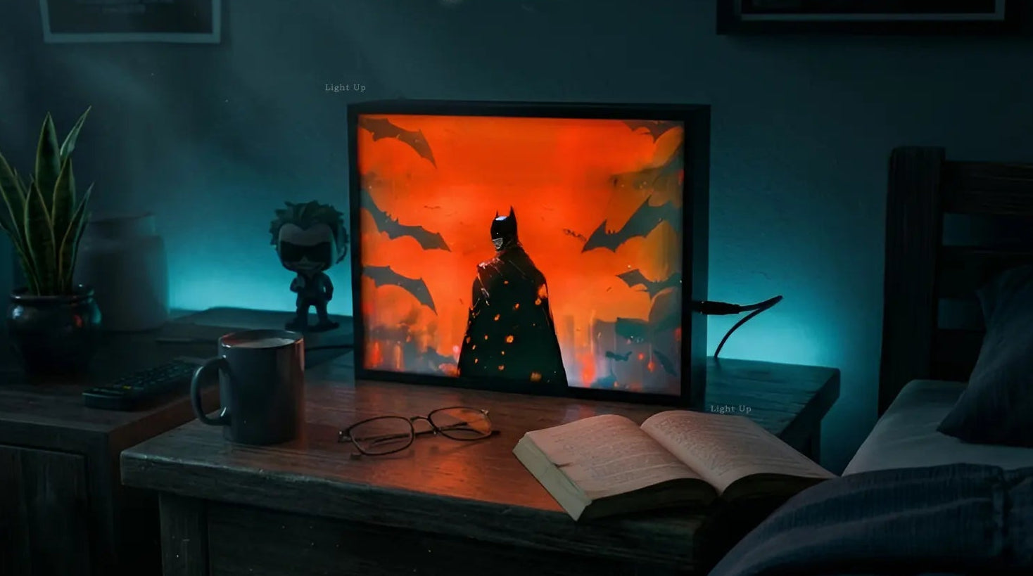 Dark room with a desk featuring a transformation lightbox displaying a batman superhero graphic, mug, and open book.